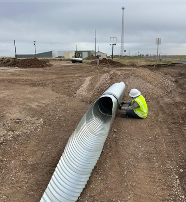 Akal Construction crew installing corrugated metal culvert pipe in an excavated trench